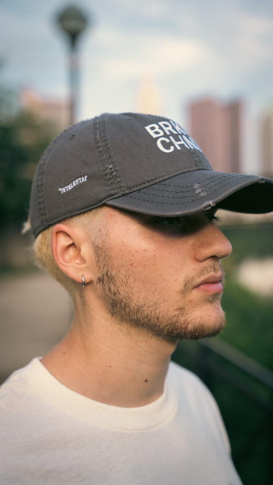 Man wearing a black cap with 'BRKN CHZNS' text, blurred background