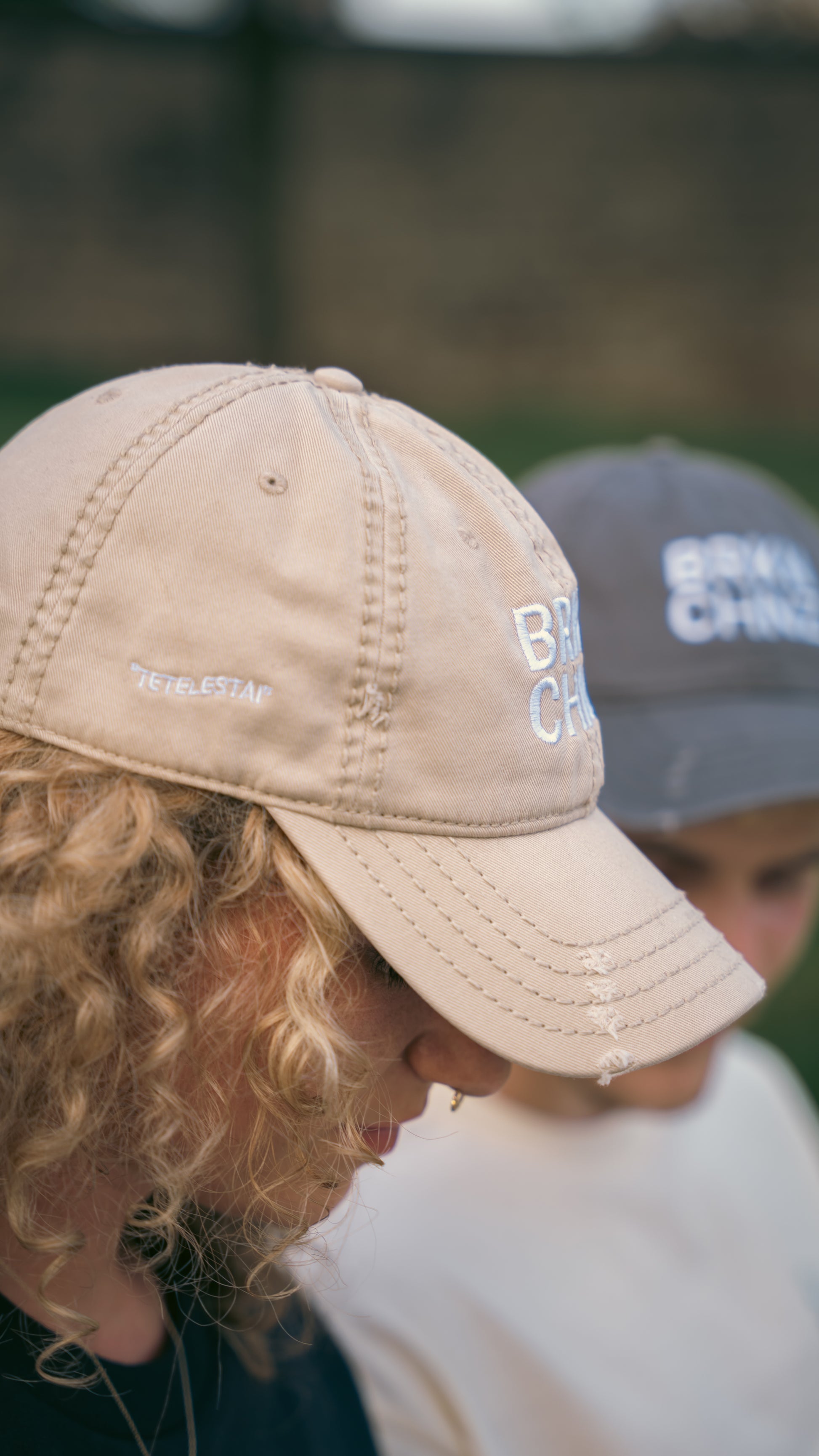 Two people wearing baseball caps with visible branding, blurred background